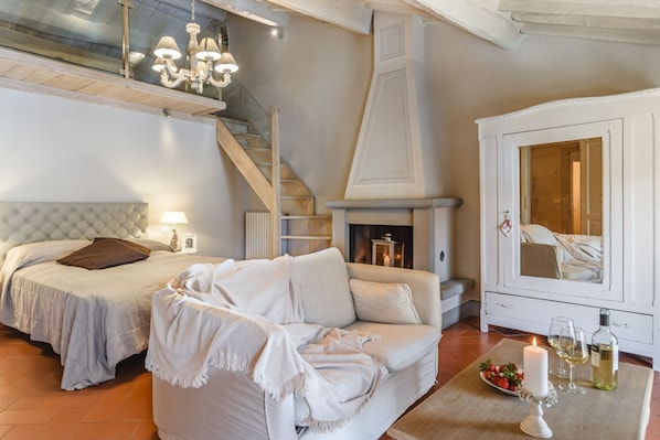 A bedroom with a bed, a sofa, a fireplace, a staircase, and a cabinet.