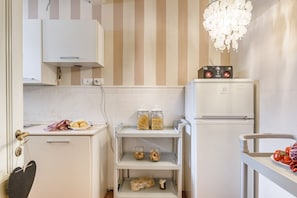 A compact kitchen with a white refrigerator, a shelf with jars, and a small countertop with food items.