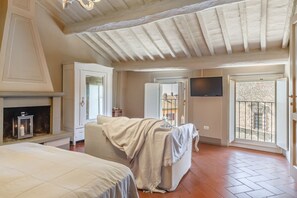 Une chambre avec une cheminée, un lit, un canapé, une télévision et un balcon avec vue.