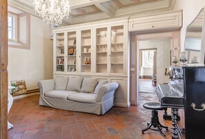 Una stanza con un divano color beige, un lampadario, un pianoforte e un'ampia credenza con ante in vetro.