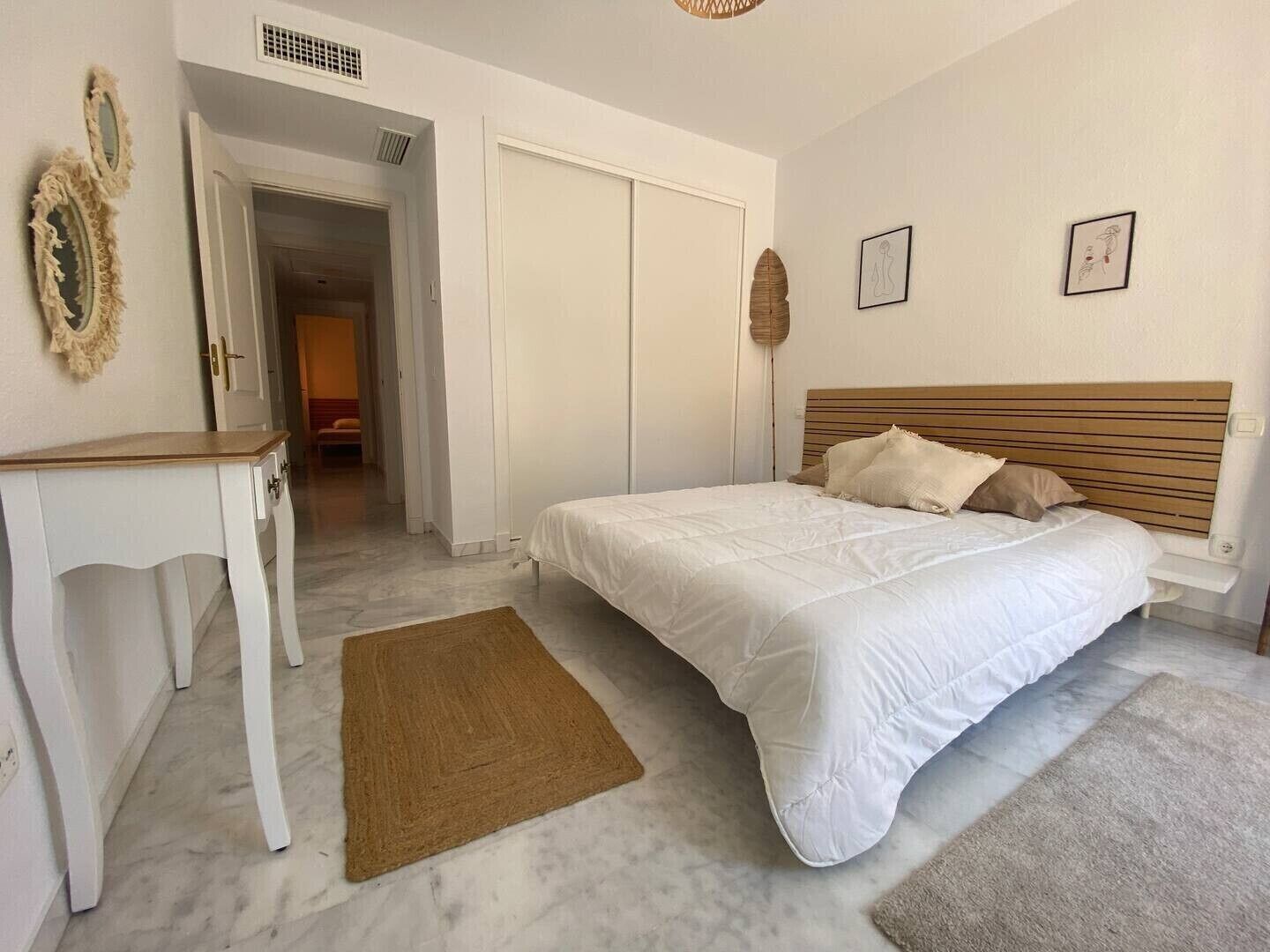 A bedroom with a bed, a bedside table, a wardrobe, and a door leading to another room.