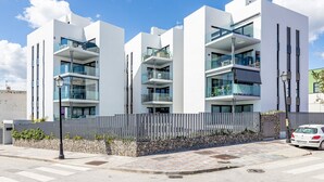 Ein modernes Mehrfamilienhaus mit Balkonen, einer Steinsichtmauer und einem gepflasterten Fußweg.