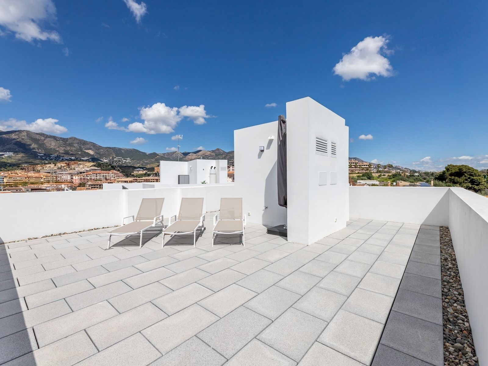 Une terrasse sur le toit, avec des murs blancs, quelques chaises longues et une vue sur un paysage montagneux.