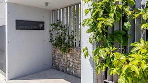 Ein begrenzter Eingangsbereich mit einem Schild, auf dem 'GARDEN HOME' steht, und eine Steinmauer mit Kletterpflanzen.