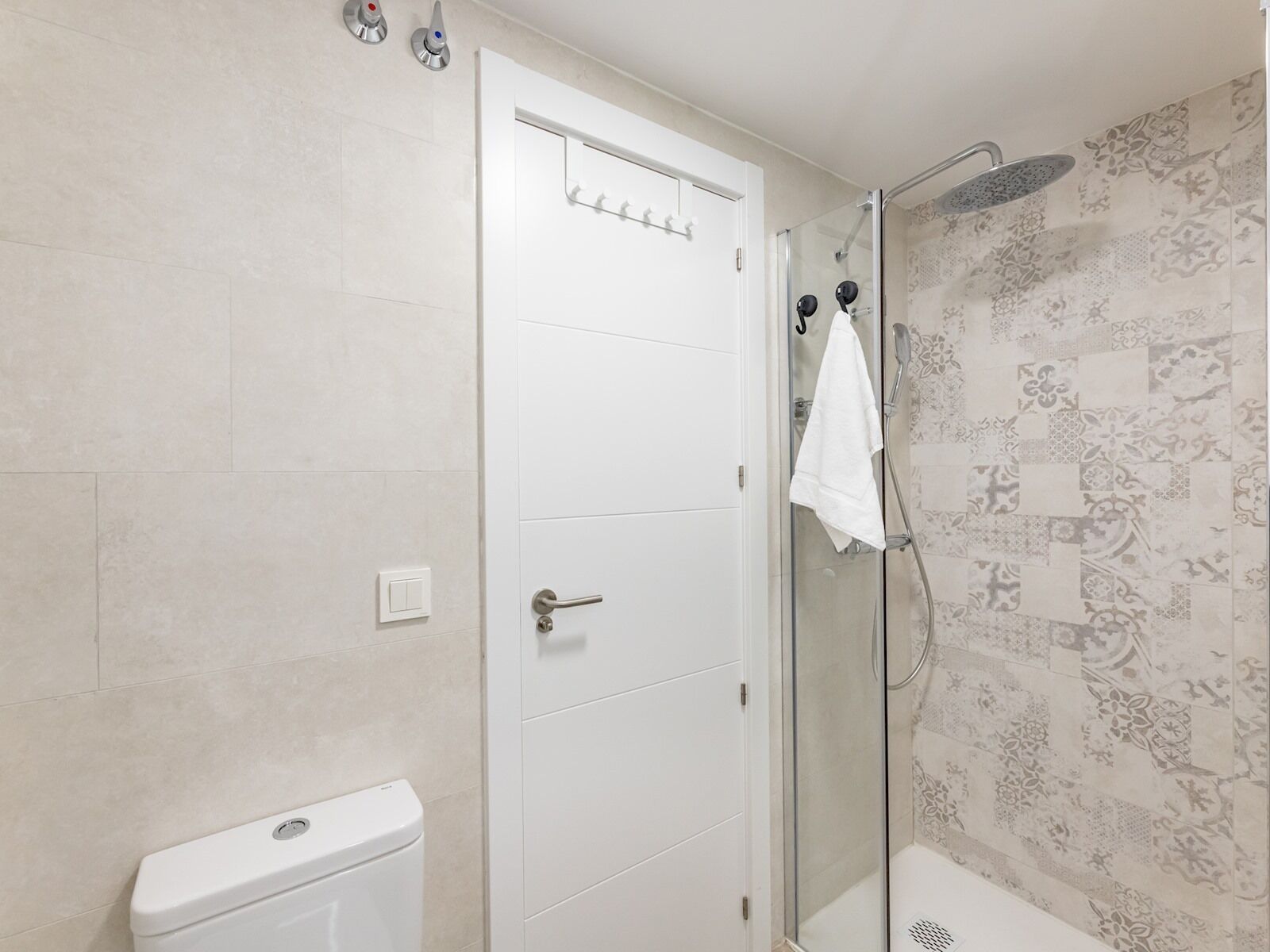 Een badkamer met toilet, douche met glazen deur en een behang met patroon.