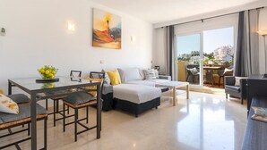 A modern living room with a sofa, chairs, a dining table, and a painting on the wall. - Stunning Views-Miraflores Apartment; Pass the Keys (Mijas)
