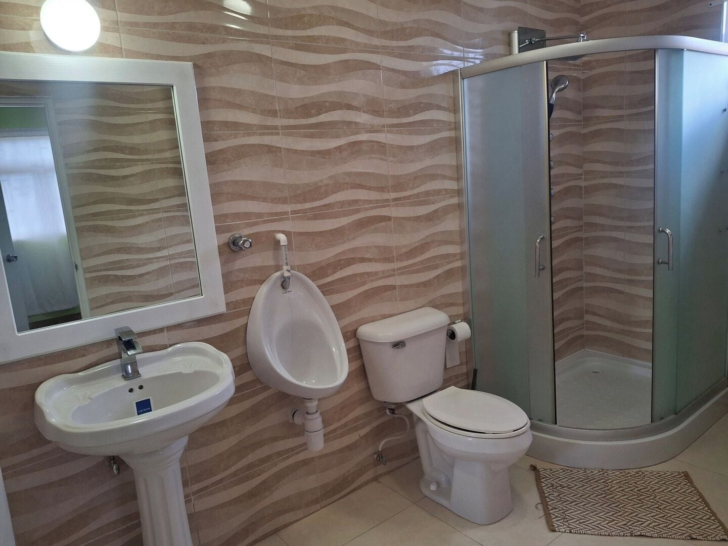 Et badeværelse med håndvask, urinal, toilet og en brusekabine med glasvægge.