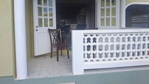 Une porte ouverte donnant sur un coin repas avec une table et des chaises, une clôture décorative blanche et une fenêtre à carreaux.