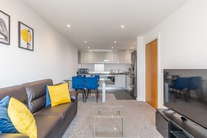 A modern living room with a sofa, TV, and a kitchen in the background.