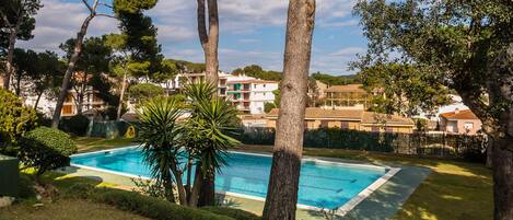 Una piscina rodeada de árboles y una zona residencial con casas al fondo.