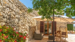 Un muro de piedra, muebles de mimbre y una zona de estar cubierta con un árbol.