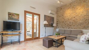 Una sala de estar con televisión sobre un mueble de madera, pared de piedra, sofá y una mesa con lámpara.