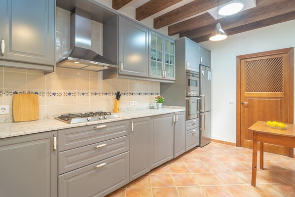 Una cocina con armarios grises, salpicadero de azulejos, estufa a gas y una mesa de madera con limones.