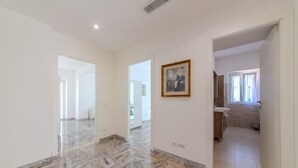 Ruime kamer met een marmeren vloer, een inlijsting foto aan de muur, en uitzicht op een andere kamer met een wastafel en kasten.
