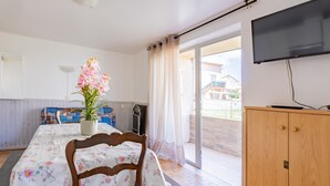 Een kamer met een houten eettafel, stoelen, een potplant, een televisie en een schuifdeur die leidt naar een buitenruimte.