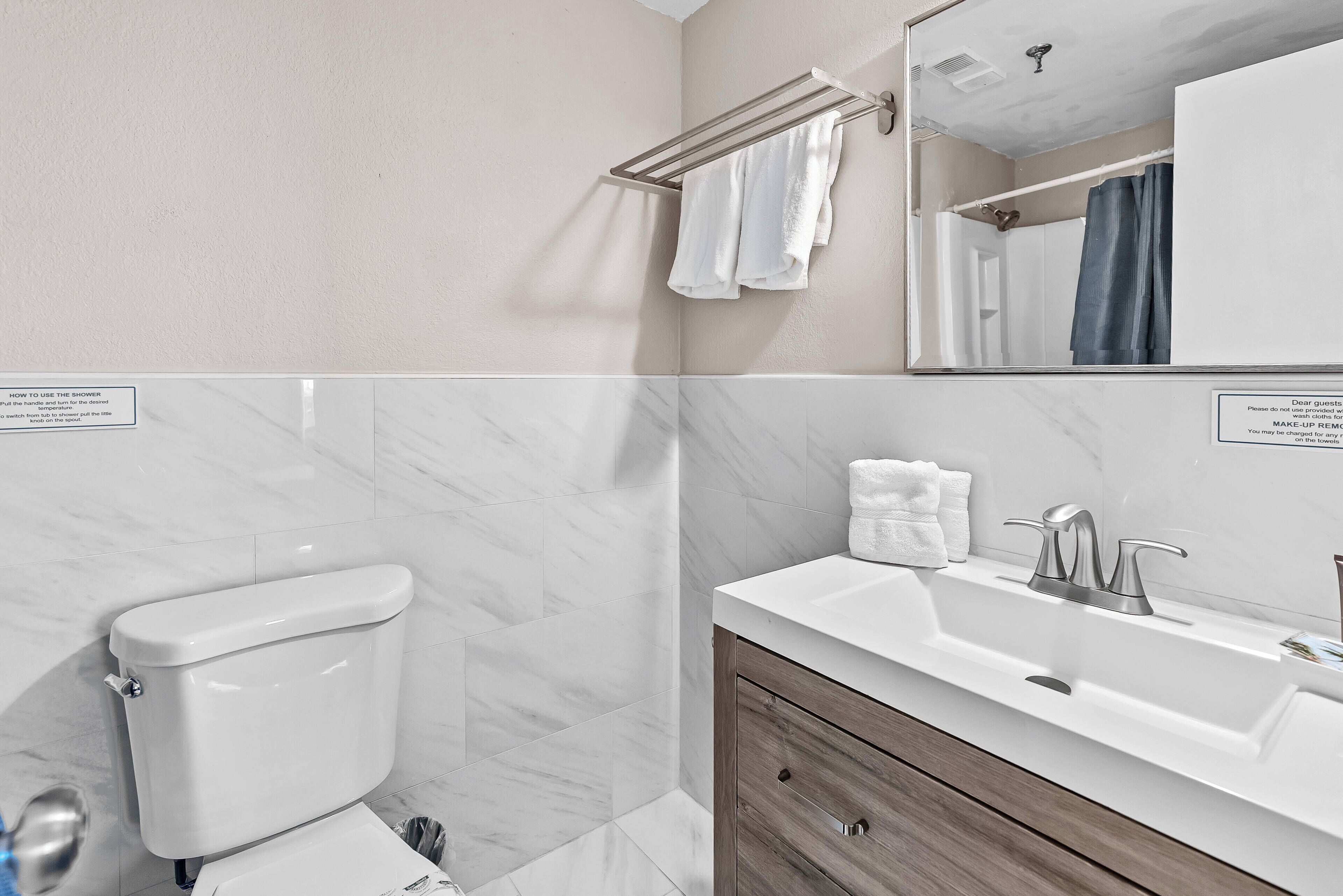 Step into this stylish bathroom featuring sleek marble walls and a chic wooden vanity. Ample natural light enhances the fresh, clean atmosphere, while carefully arranged towels add a touch of comfort and convenience for your stay.