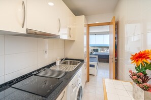 Moderni keittiö, jossa on sisäänrakennettu uuni, ruostumattomasta teräksestä valmistettu allas ja näkymä olohuoneeseen.