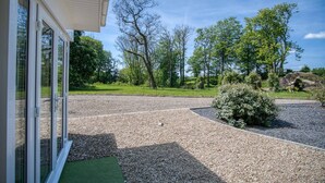 Une allée de gravier mène à une maison, avec une pelouse verdoyante et des arbres en arrière-plan.