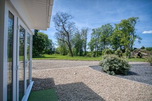 A gravel driveway leading to a house with a green lawn and trees in the background.