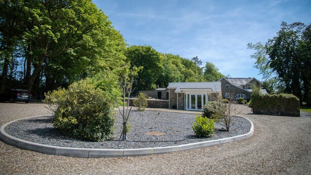 Un bâtiment en pierre au design moderne, entouré d’une allée gravillonnée et de petits arbres.