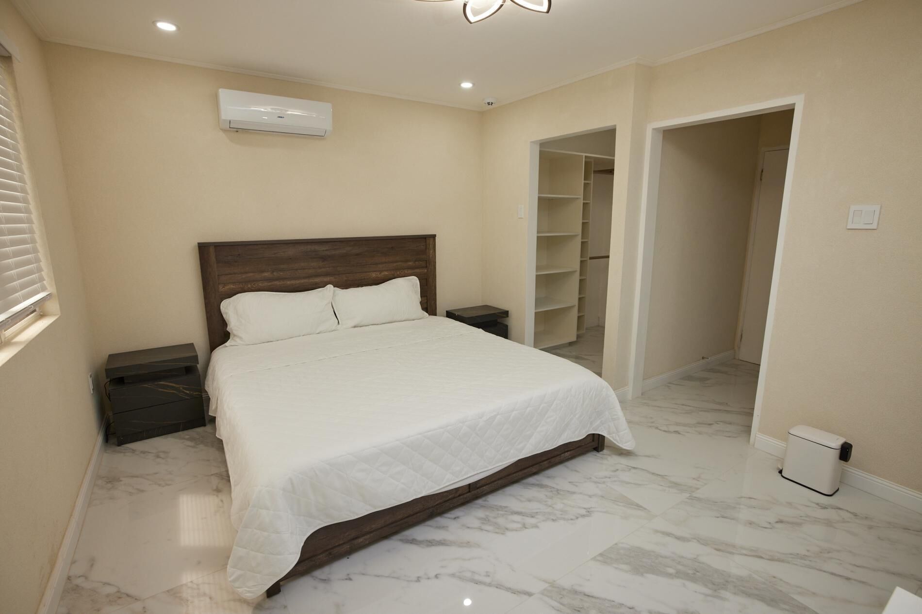 A bedroom with a bed, nightstands, a wardrobe, and an air conditioning unit.