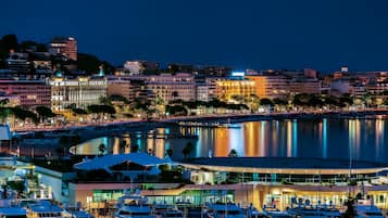 Un port de plaisance avec des bateaux, une promenade en bord de mer et des bâtiments aux façades illuminées.