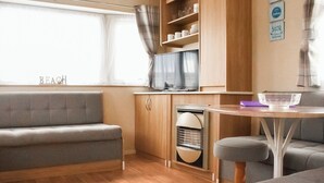 A compact living space with a sofa, a small table, a television, and a cabinet. - Introducing the ABI Vista, a 2-bedroom caravan designed to accommodate up to 6 guests. (Caister-on-Sea)