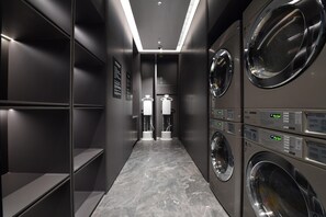 Une buanderie moderne équipée de plusieurs machines à laver et de plusieurs sèche-linge, avec un sol carrelé et un couloir étroit.