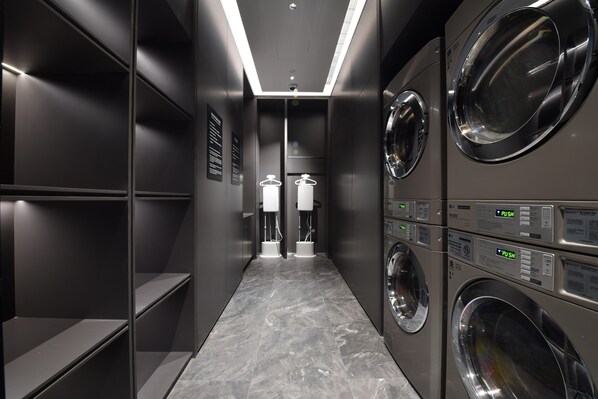 A modern laundry room with multiple washing machines and dryers, a tiled floor, and a narrow hallway. - City Inn Shanghai Xizang South Road Hotel (Shanghai)