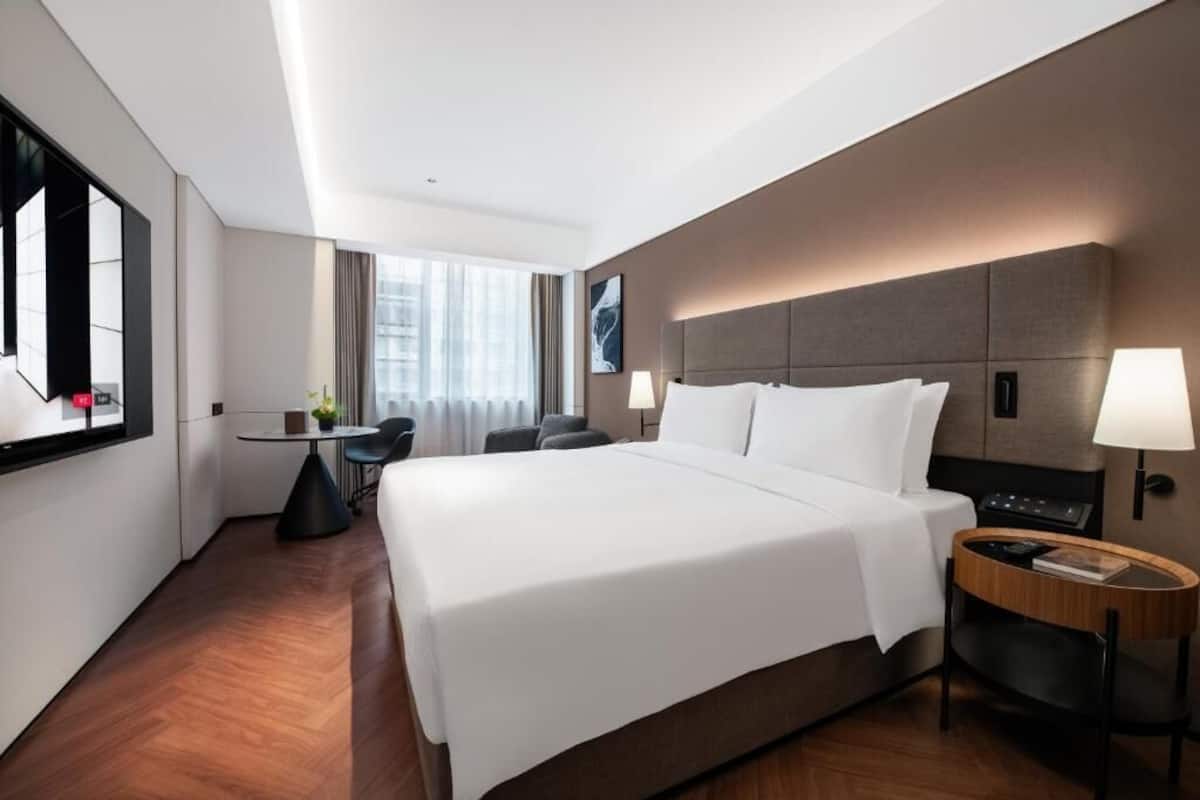 A modern hotel room with a large bed, a desk, and a chair.