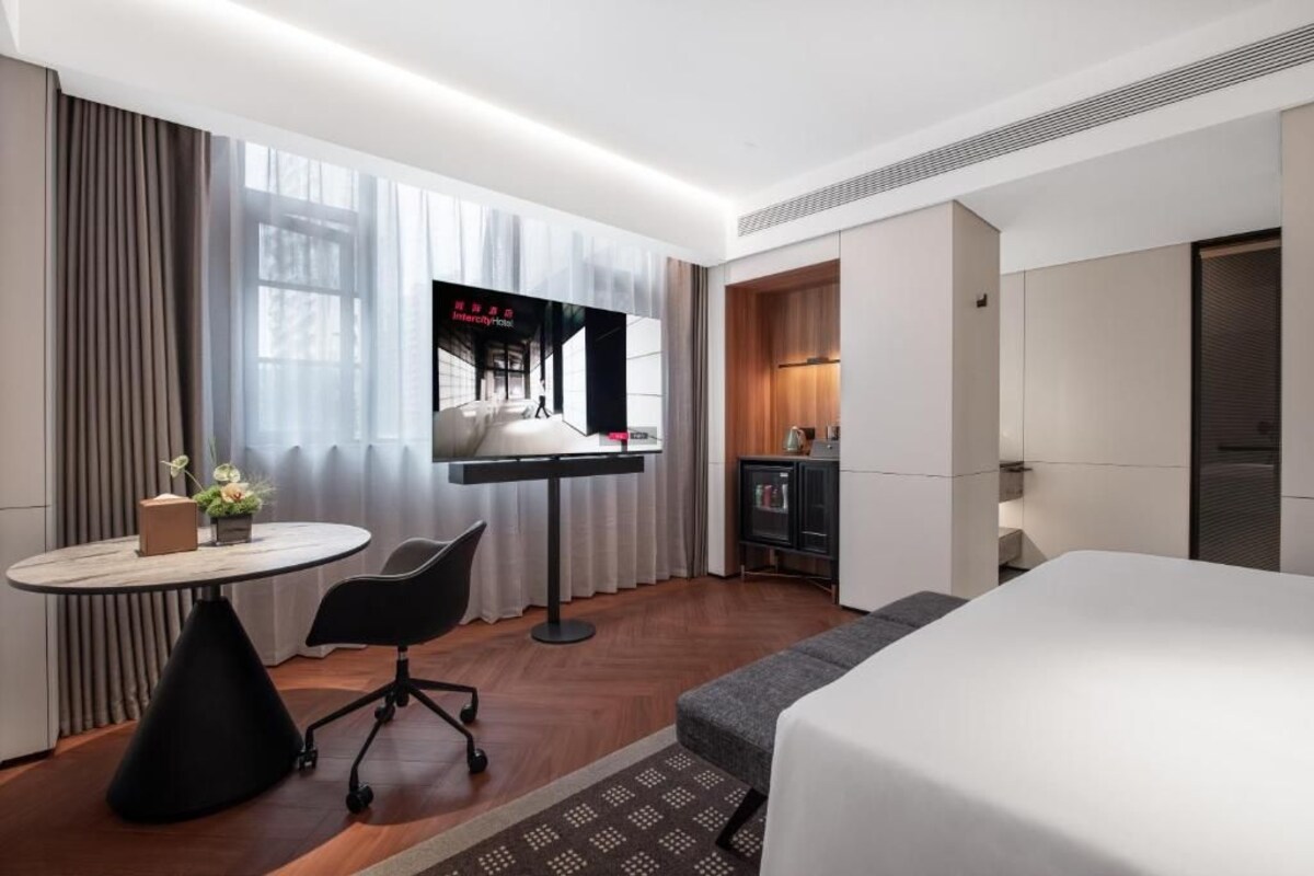 A hotel room with a bed, a desk with a chair, a television, and a small table with a vase of flowers.