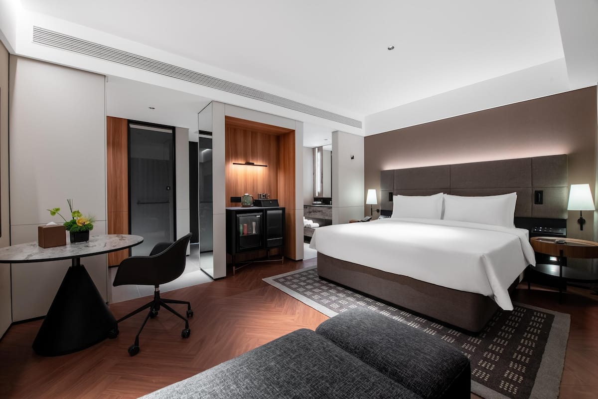 A modern hotel room with a large bed, a desk, and a kitchenette.
