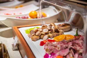 Un buffet proposant une variété de plats, notamment des viandes en tranches, des saucisses et des fruits.