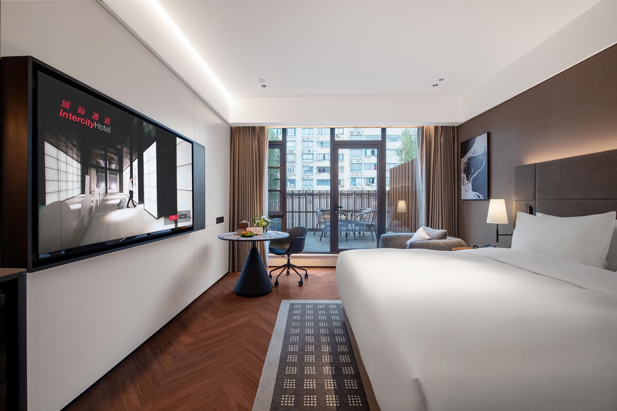 Une chambre d’hôtel équipée d’un lit, d’un bureau, d’une chaise, d’une télévision et offrant une vue sur l’extérieur.