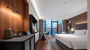 A modern hotel room with a bed, a desk with a kettle, a small table, and a view of the city through large windows. - City Inn Shanghai Xizang South Road Hotel (Shanghai)