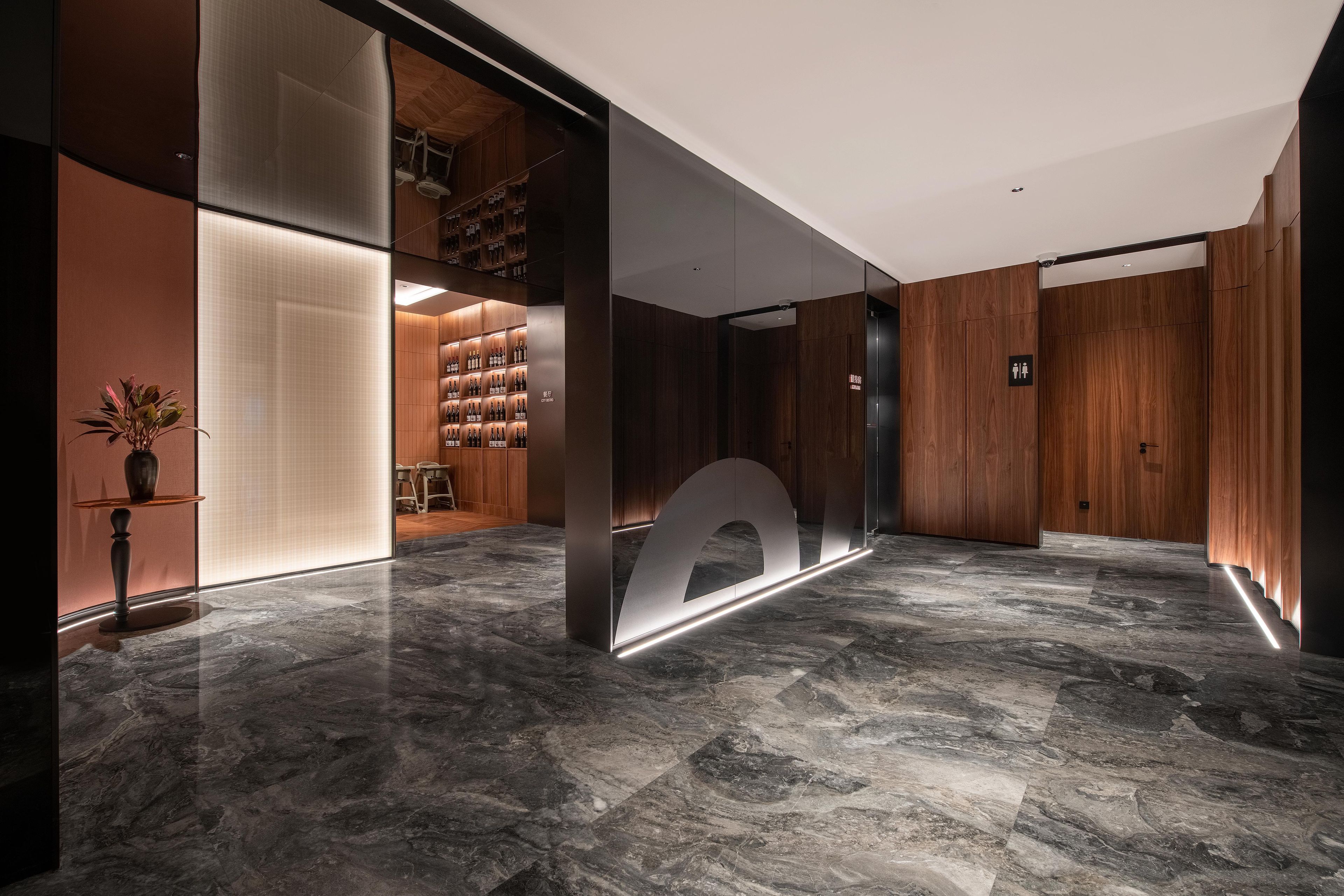 A modern hotel lobby with a marble floor, wooden paneling, and a glass partition with a circular cutout.