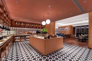 Un restaurant moderne doté d’un îlot central, d’étagères en bois où sont disposés des bocaux, et d’un sol à motifs.