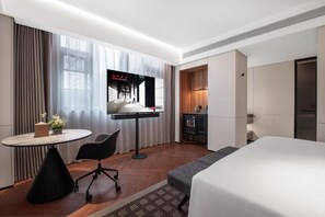 A hotel room with a bed, a desk with a chair, a television, and a small table with a vase of flowers.