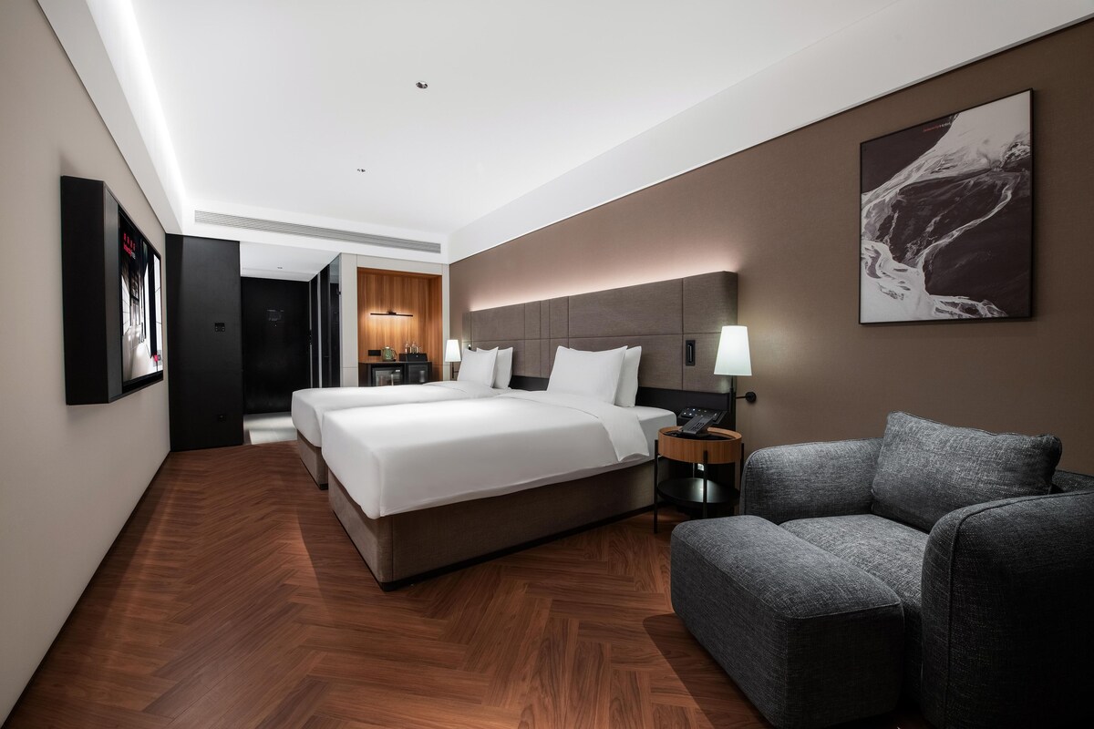 Ein modernes Hotelzimmer mit einem großen Bett, einer Couch, einem Schreibtisch mit Lampe und einem Wandbild.