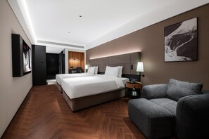 Ein modernes Hotelzimmer mit einem großen Bett, einer Couch, einem Schreibtisch mit Lampe und einem Wandbild.