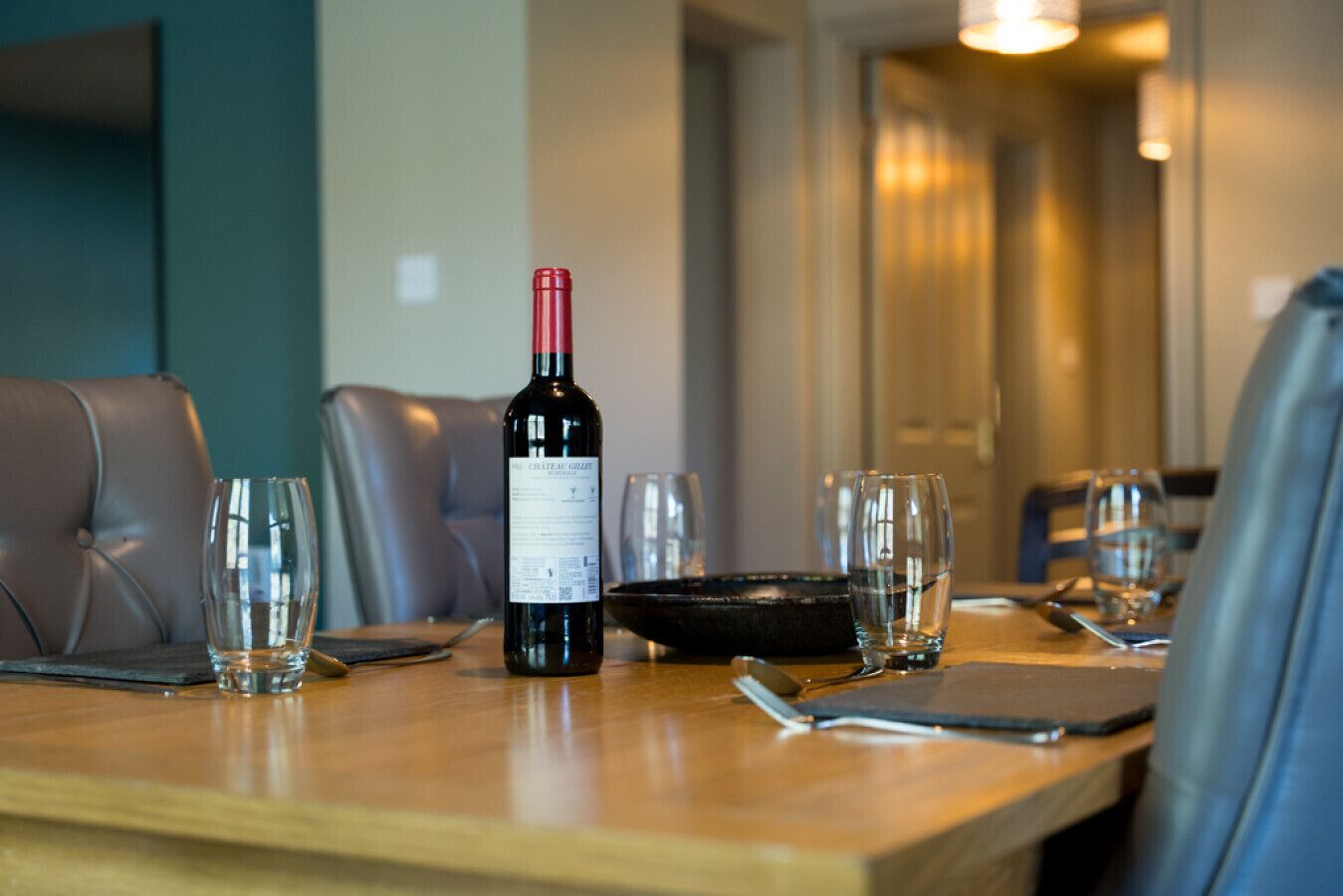 A dining table set with a bottle of wine, glasses, and cutlery.