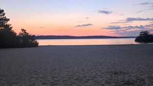 Una playa con un cuerpo de agua tranquilo, árboles y una costa distante.