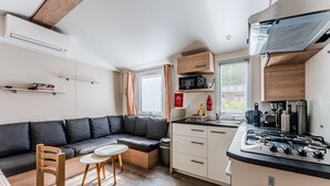 Un espacio habitable compacto con kitchenette, sofá, zona de comedor y ventana con cortinas.