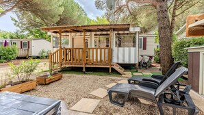Un espacio al aire libre cubierto con piso de madera, un pequeño edificio con una ventana, y un patio de grava con sillas de lounge.