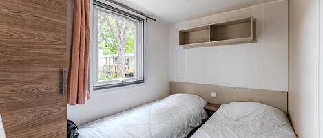 Un dormitorio con dos camas, una ventana con cortinas, un armario de madera y una repisa sobre las camas.