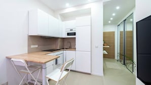 A compact kitchen with white cabinets, a wooden countertop, and a small dining area with two chairs.