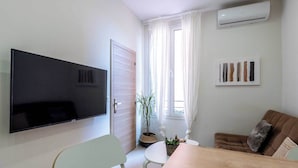A modern living room with a flat-screen TV, a dining table, a couch, and a potted plant.