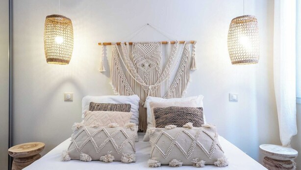 A bedroom with a bed, macramé wall hanging, and two hanging light fixtures.