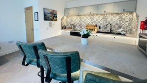 A modern kitchen with a central island, built-in appliances, and a patterned backsplash. - Bramble Apartment in Fort William Town Centre (Fort William)