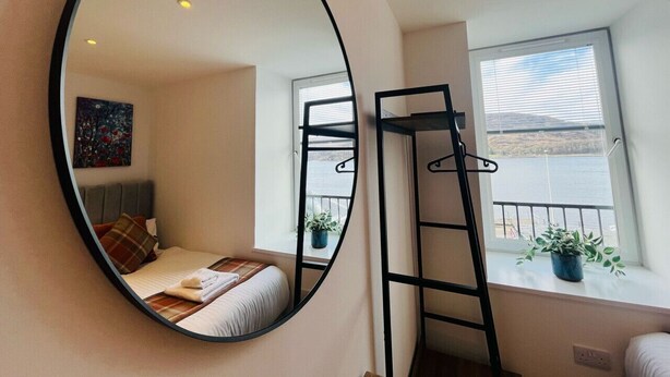 A bedroom with a bed, a mirror, a window with a view of the sea, and a ladder. - Bramble Apartment in Fort William Town Centre (Fort William)